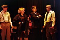 A man with a moustache addressing two men, one with his arms crossed, and a woman