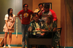 A man and a woman sit at a desk, while a young woman, a man in a red Avengers T-shirt, a man in a suit,
        and a man in a Tampa Bay Buccaneers T-shirt look on behind them