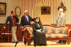 Holmes, the bald man with the head bandage and Dr. Watson stand while the woman in the dark gray dress and
       blue blouse sits on the couch